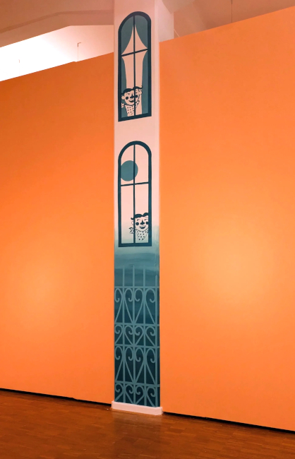 Eine Betonsäule ist mit den Bildern von einem Metallzaun und zwei Fenstern, aus denen comicartige Figuren schauen, gestaltet.