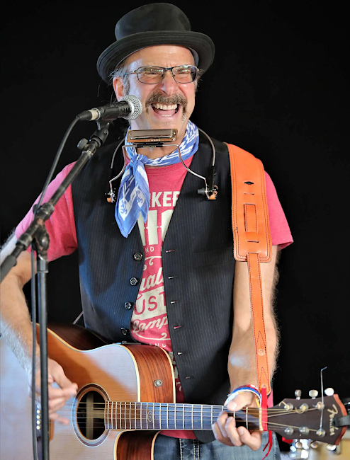 Foto des lachenden Sängers bei einem Auftritt mit Gitarre vor einem Mikrofon.