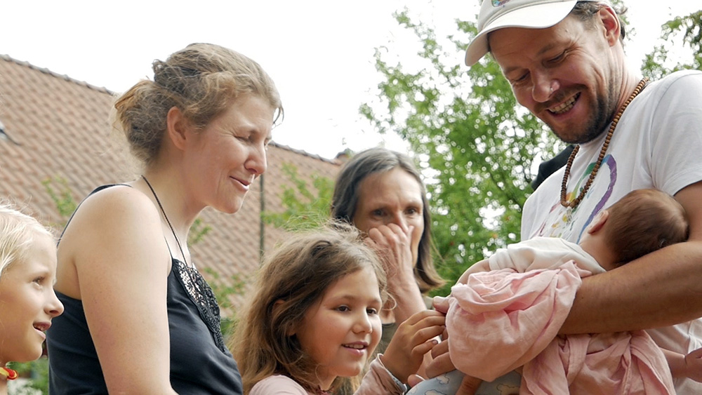 Filmszene in der ein junger Vaterden Dorfbewohnern sein Baby zeigt.