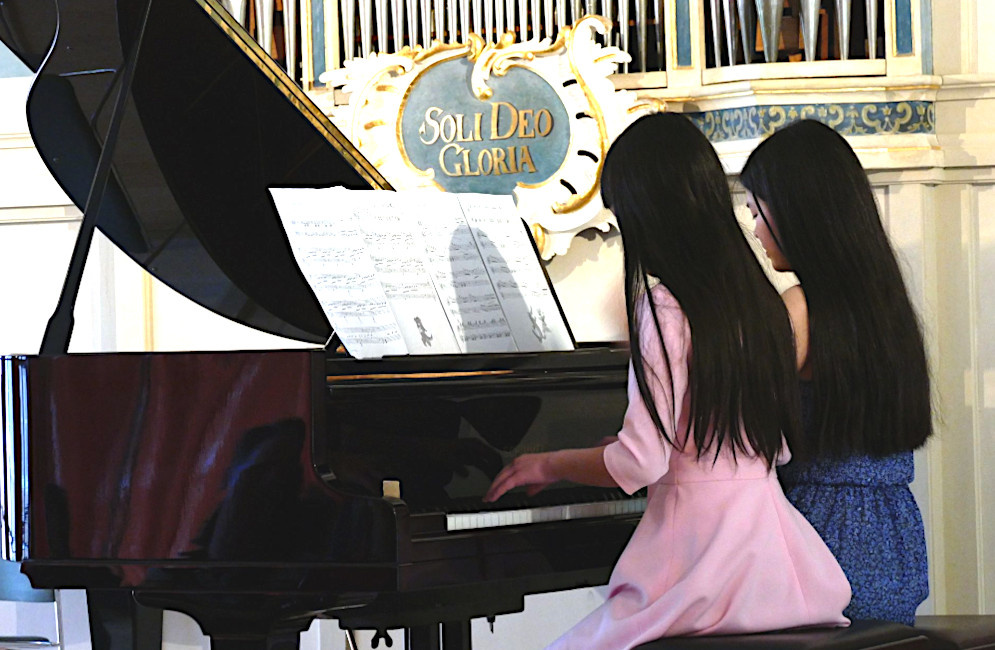 Zwei Mädchen spielen nebeneinander auf einem Konzertflügel.