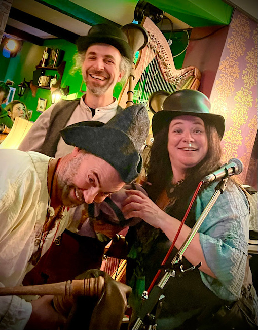 Eine Sängerin und zwei Musiker in historischer Kleidung lachen fröhlich in die Kamera.