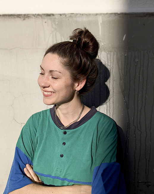 Die Künstlerin lächelt mit geschlossenen Augen in der Sonne.