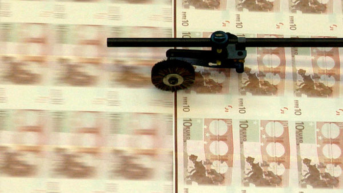 Foto einer Druckmaschine für Banknoten, auf der große Bögen mit Geldscheinen zu sehen sind, die noch nicht auseinander geschnitten sind.
