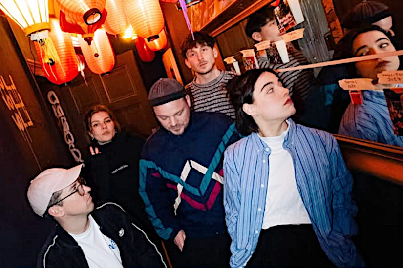 Foto der Band in einem kleinen Raum mit Spiegeln