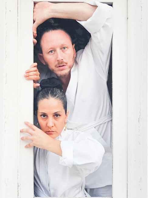 Das Duo trägt Judoanzüge und blickt ernst aus einem weißen Fenster