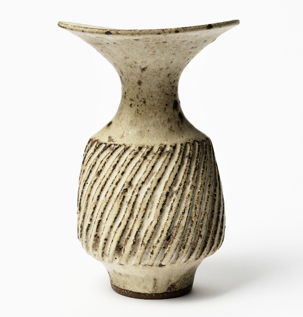 Eine kleine Vase aus beigen Material mit dunklen Punkten und schrägen Kerben als Dekor