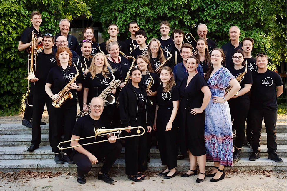 Gruppenfoto der lächelnden Musikerinnen und Musiker mit ihren Instrumenten auf einer Treppe im Freien