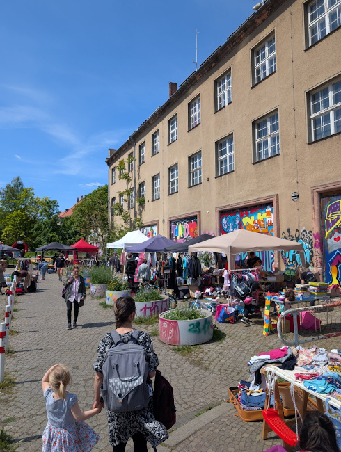 Vor einer ehemaligen Feierwache mit bunt bemalten Toren sind viele Stände und Pavillons zu sehen.