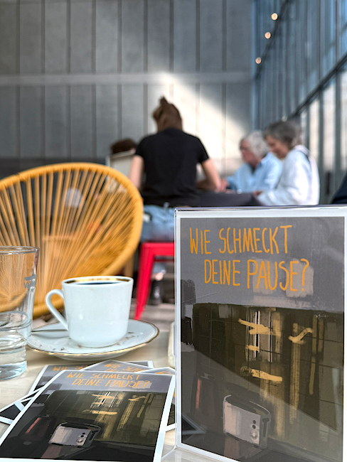 Im Museumscafé des MdbK stehen und liegen auf einem Tisch neben einer Tasse Kaffee Postkarten mit der Aufschrift "Wie schmeckt deine Pause?" und dem Foto eines Toasters.