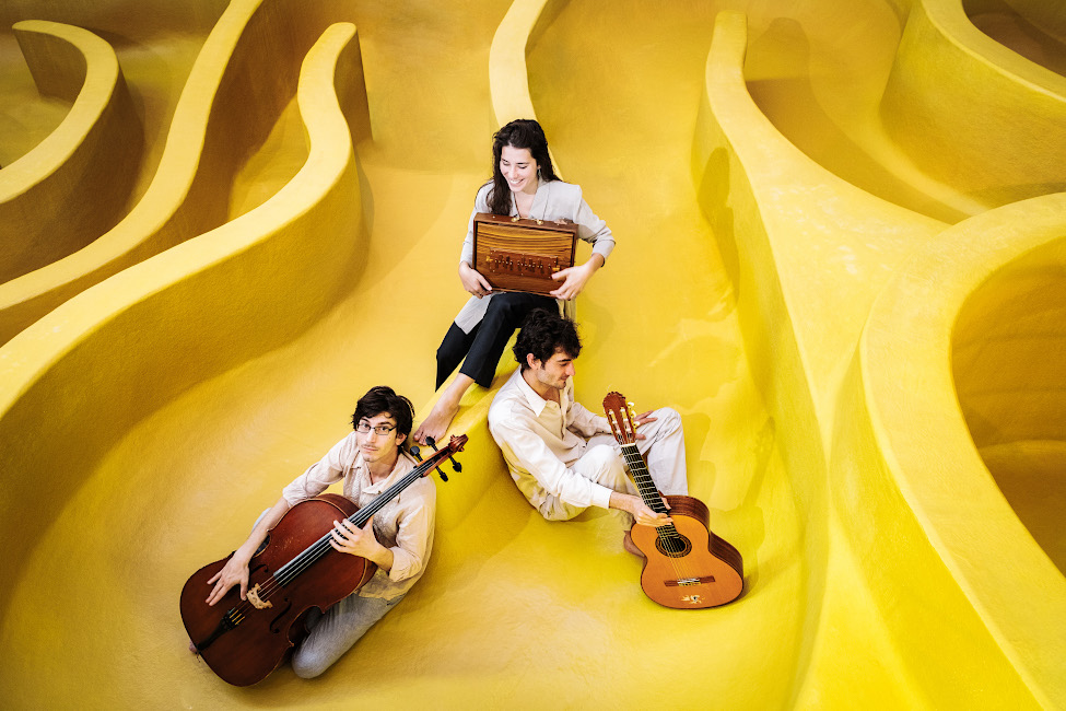 Gruppenfoto des Trios mit seinen Instrumenten in einem zitronengelben Labyrinth