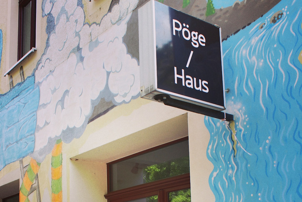 Ein Leuchtkasten mit der Aufschrift "Pöge / Haus" an der bunt bemalten Fassade des Hauses