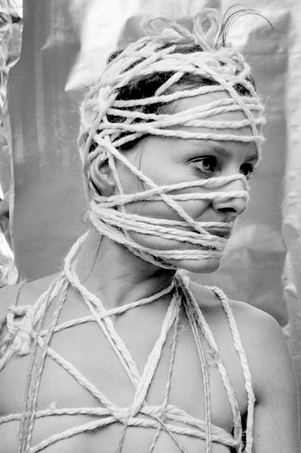 Eine junge Frau hat ihr Gesicht und ihren Körper mit Stricken umwickelt.