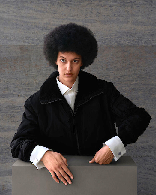 Porträtfoto der Künstlerin vor einem grauen Hintergrund, auf dem die Hände besonders hervorgehoben werden.