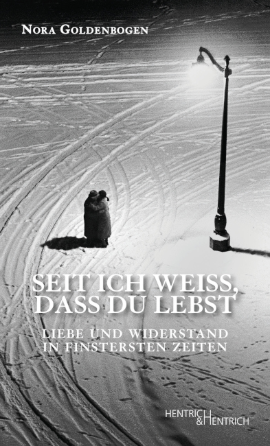 Zwei Personen stehen fest umarmt nachts im Winter unter einer Laterne.