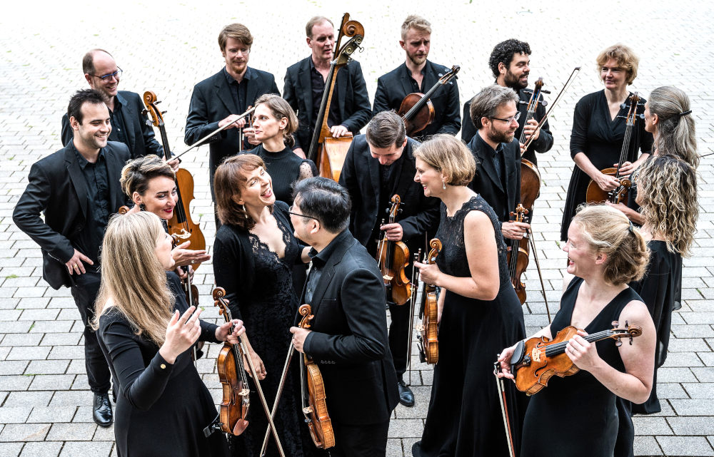 Die vier Musikerinnen und Musiker stehen mit ihren Instrumenten auf einem Platz und unterhalten sich angeregt.