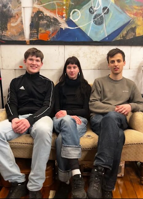 Gruppenbfoto des freundlich lächelnden Trios auf einem Sofa.