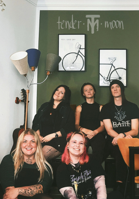 Gruppenfoto in einem Wohnzimmer vor einer grünen Wand, an der "Tender Moon" steht.
