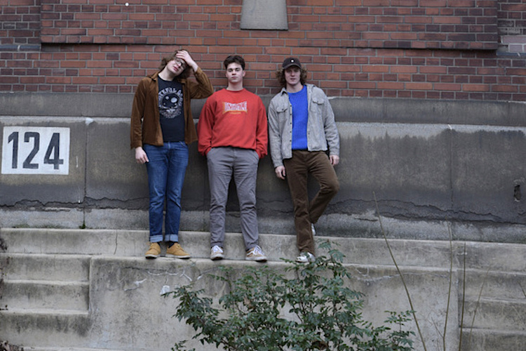 Gruppenfoto der drei jungen Musiker vor der Ziegelwand eines alten Fabrikgebäudes