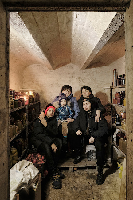 Foto einer Familie, die in einem Keller zwischen Regalen mit Konserven sitzt