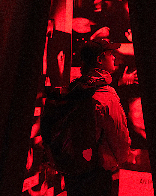 Eine Personmit Rucksack betritt durch einen Vorhang eine rot ausgeleuchteten Raum.