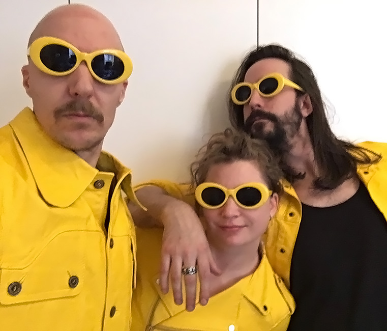Gruppenfoto des Trios mit gelben Jacken und Sonnenbrillen