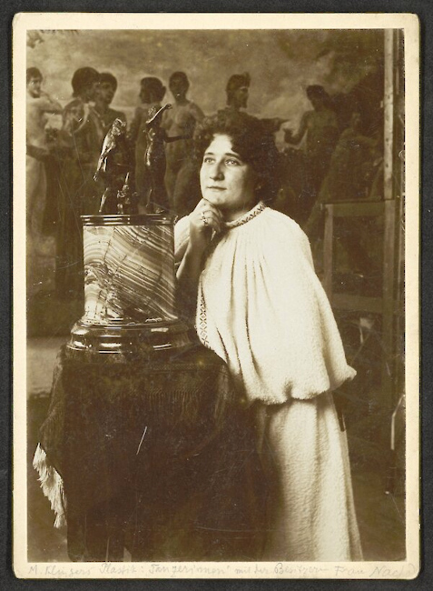 Historisches Foto einer Frau, die sich eine kleine Skulptur auf einem hohen Sockel anschaut - im Hintergrund ist ein großes Gemälde zu sehen